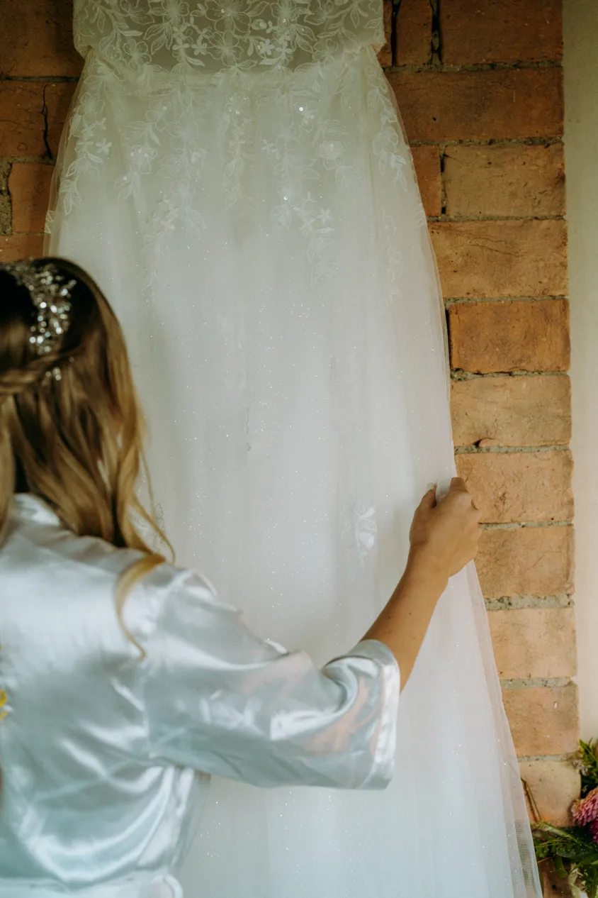 Braut im Satinmantel berührt ihr hängendes Brautkleid