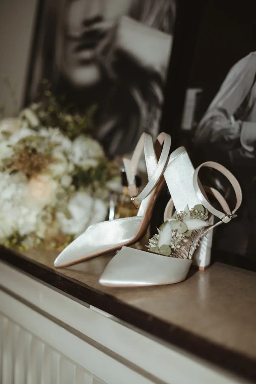 White bridal shoes with dried flowers beside bouquet