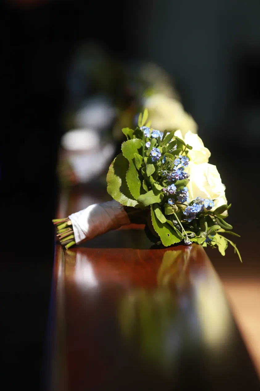 Brautstrauß mit weißen Rosen auf glänzender Holzbank im Sonnenlicht